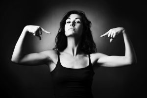 Woman demonstrating her muscles and pointing to herself. Black and white studio portrait